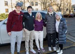 A group of people stand together, smiling at the camera in front of a vehicle.