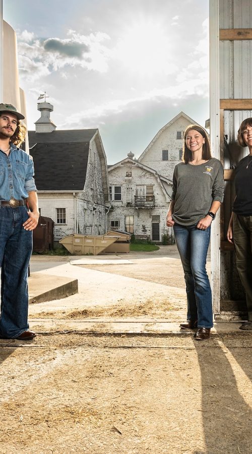 Three undergraduate students stand just inside the door of a dairy barn on the campus of UW–Madison